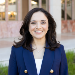 headshot of UCLA Executive MPH graduate Maite Medina. She has shoulder length brown hair and she wears a navy blue blazer over a white top.