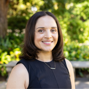 EMPH Student Maite Medina stands outside near a green-leafed tree. She wears a sleeveless black top and a silver necklace.