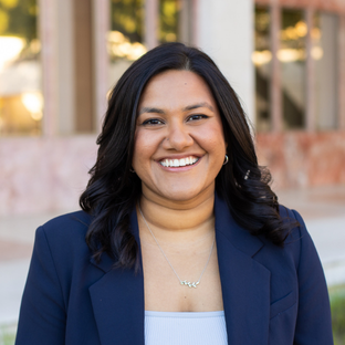 headshot of UCLA Executive MPH graduate Trishna Singh. She stands outdoors wearing a dark blue blazer over a white top. She has long dark brown straight hair.