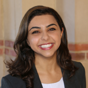 Nahal Sabrkhani stands outside on the UCLA campus against a brick wall. She has long dark hair and is wearing a black blazer over a white t-shirt