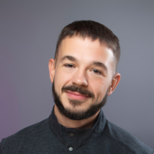 Headshot of UCLA EMPH Candidate Andy Short against a grey background. He is wearing a black shirt. He has short dark brown hair, moustache, and beard.