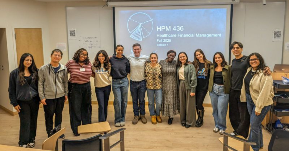 A group photograph of UCLA Executive MPH Professor Linda Magara Horner and her Healthcare Financial Management students standing in a classroom on the last day of the Fall 2025 quarter. The professor and 12 students are smiling and posing in front of a projection screen that displays "HPM 436 Healthcare Financial Management Fall 2025 Session 7" and a simple pie chart graphic. The students are diverse.