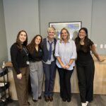 UCLA ExecHPM Staff Johanna Arias, Jenna Mendoza, Julie Carafelli, Kyle Sullivan, and Sarah Tran stand smiling in a UCLA conference room