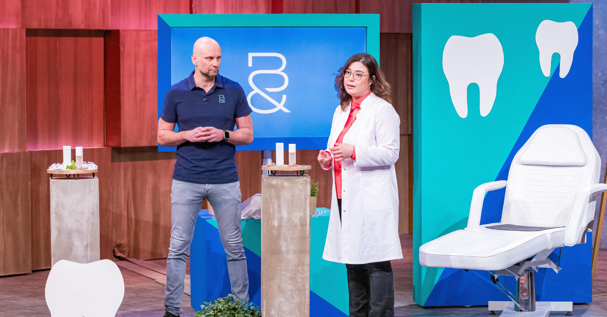 Dr. Dana Adyani-Fard, wearing a white lab coat, presents the Blessand Intensive Serum No. 7 alongside a colleague on the set of the TV show Die Höhle der Löwen. The set features dental-themed decor, including a white dental chair, large tooth cutouts, and the Blessand logo on a digital screen.