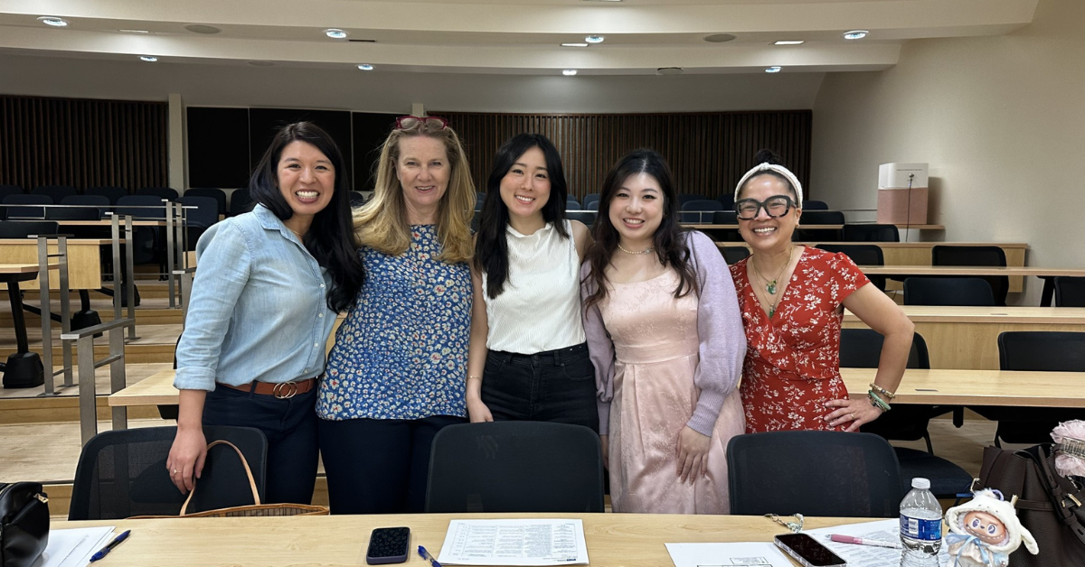 Group photo of three UCLA MHA graduates standing with MHA Program Director Dr. Laura Erskine inside a UCLA lecture hall