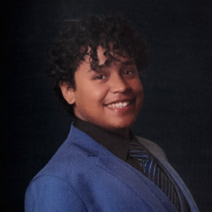 headshot of UCLA Executive MPH student Christopher Aldair Silva. He is wearing a blue blazer over a black shirt and stands against a black background. He has short curly brown hair.
