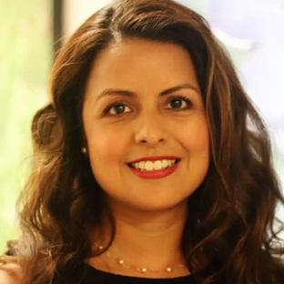 Headshot of UCLA EMPH student Raquel Vasquez. She has long wavy brown hair parted on the side. She is smiling and is wearing a chain and pearl necklace and a sleeveless black shirt.