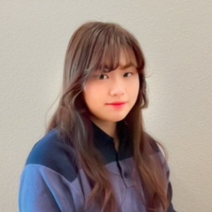 headshot of UCLA EMPH student Mika Chiang. They have long brown hair and bangs and are wearing a blue fleece pullover sweater